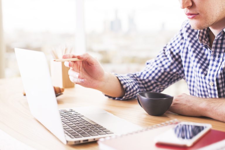 Person pointing at a laptop screen with a pencil while checking a website
