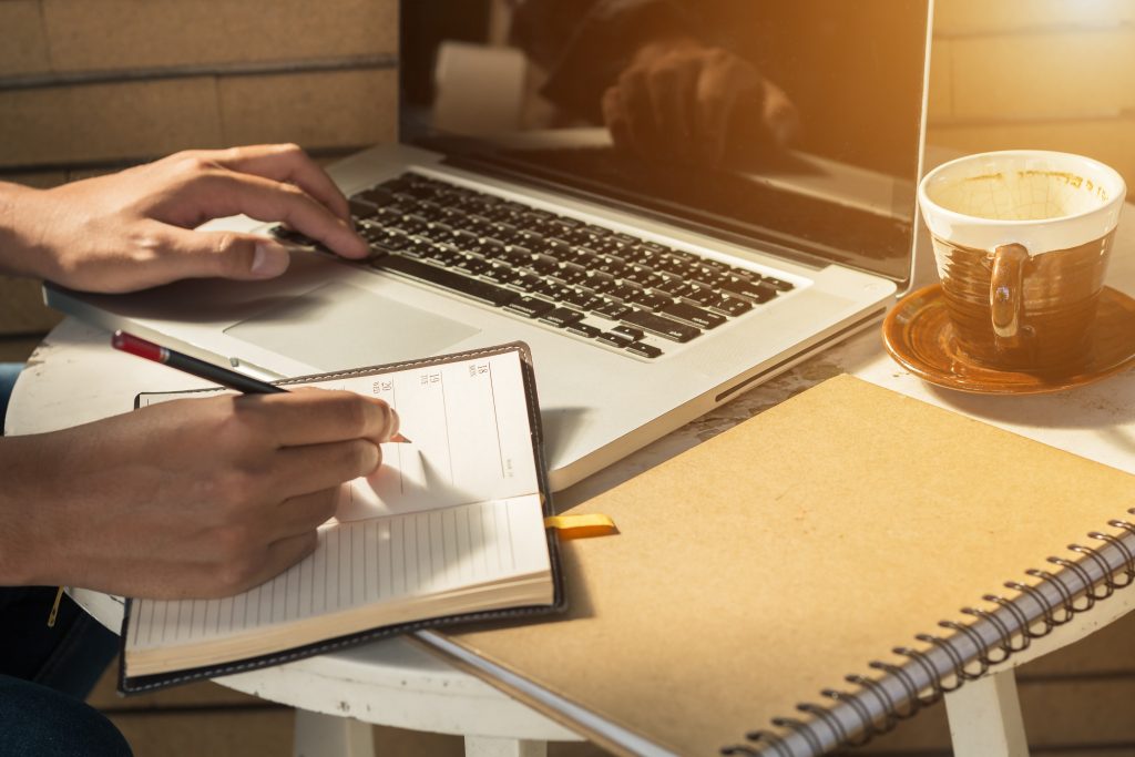 Hands using a laptop and notebook while planning a business blog post
