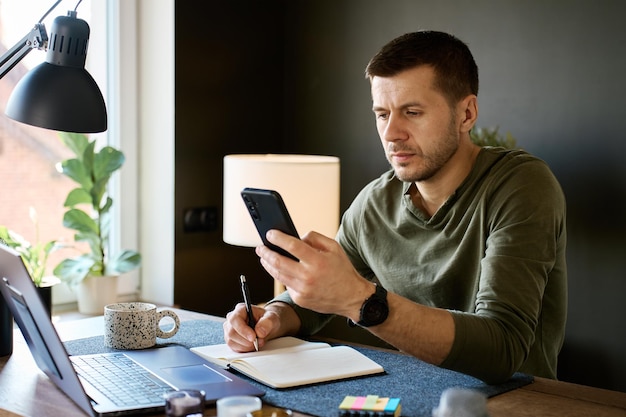 Person using a smartphone while writing notes at a desk