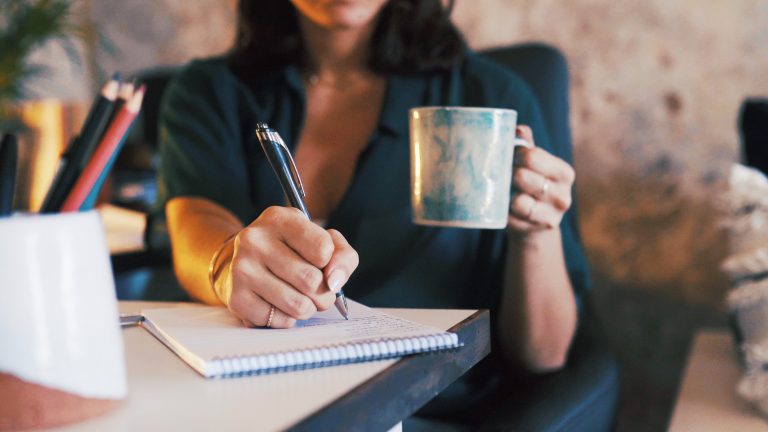Person writing notes beside a cup of coffee
